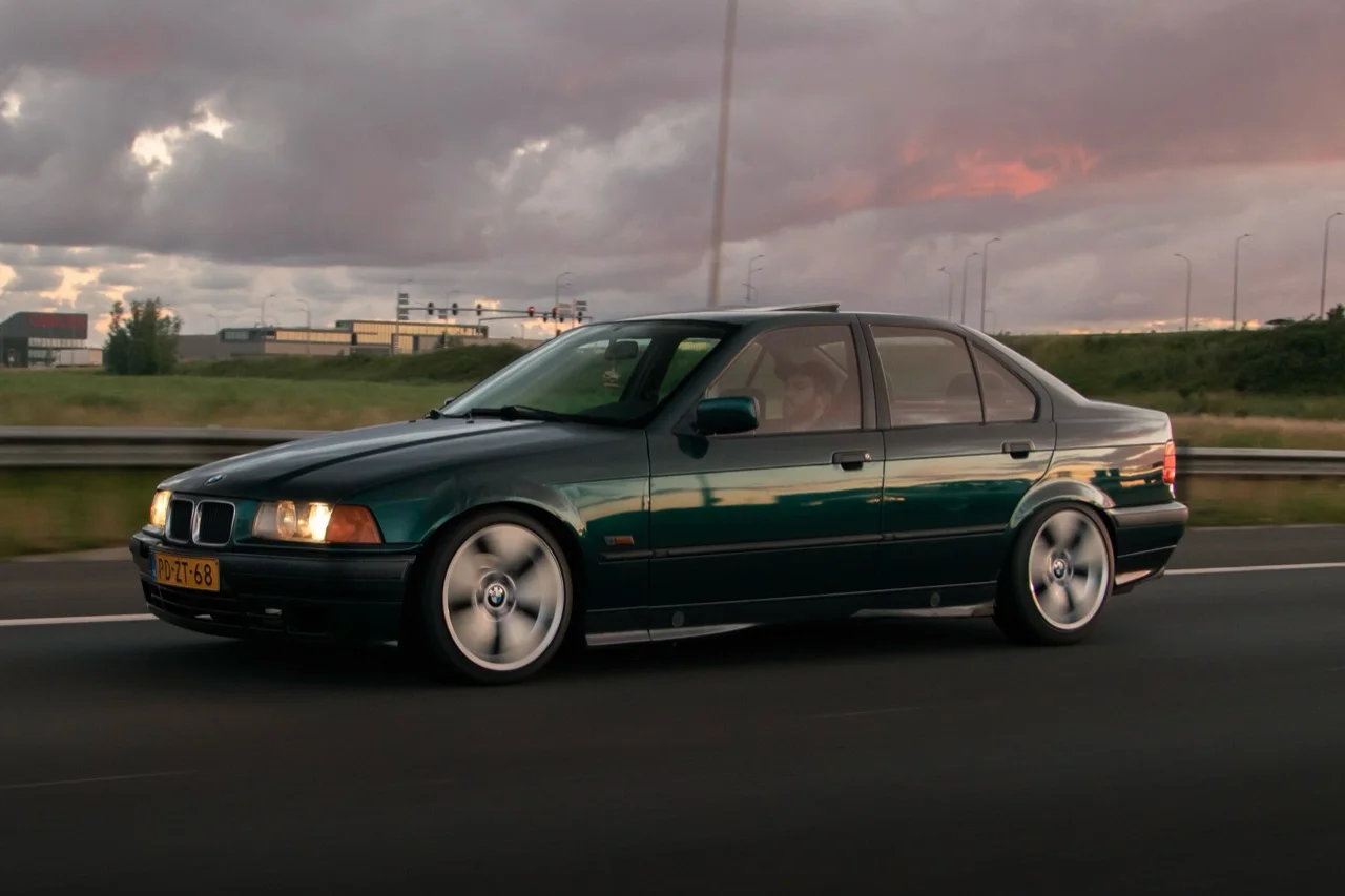 Groene BMW E36 rijdend op de snelweg bij zonsondergang